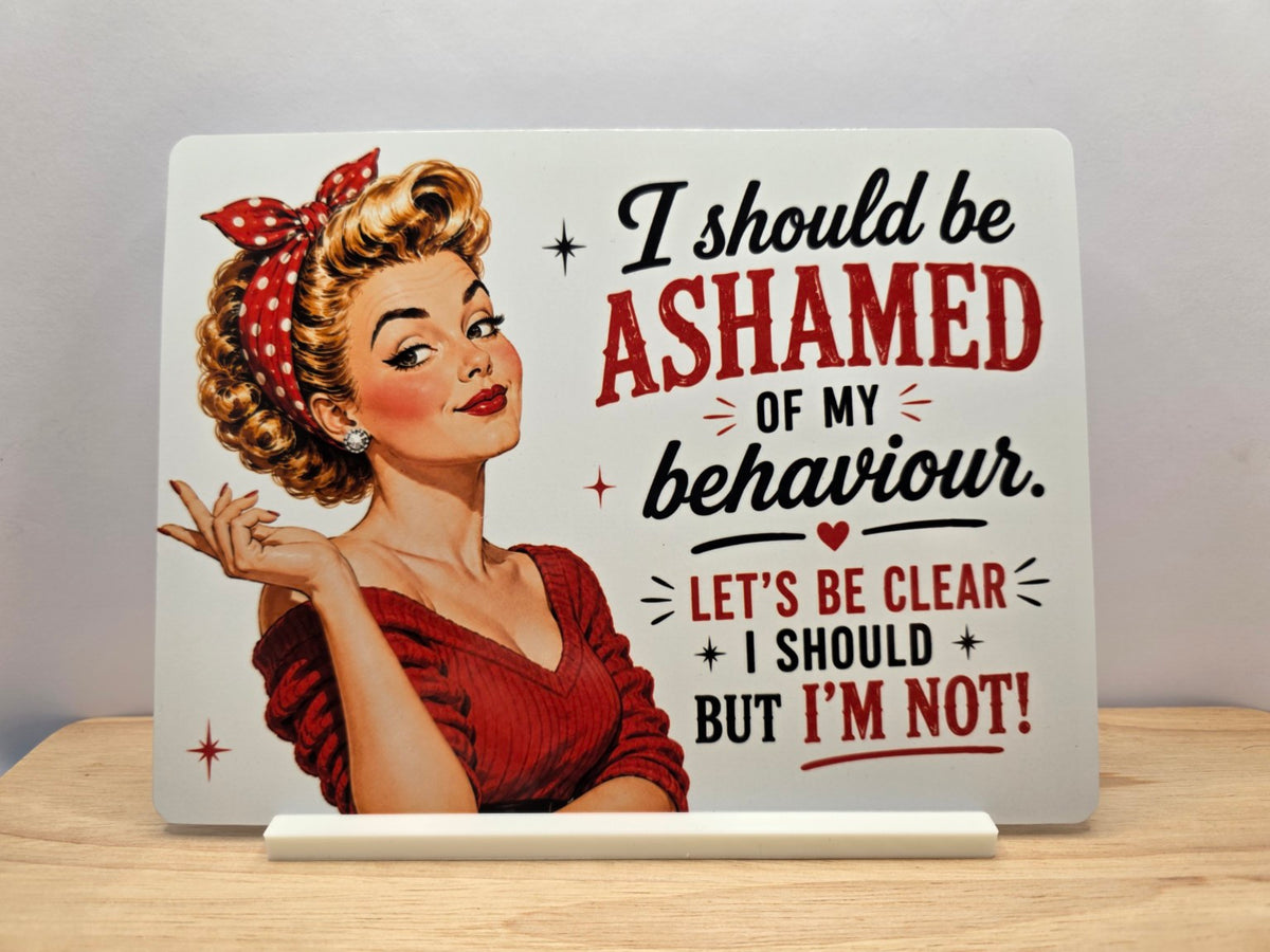 I Should Be Ashamed of My Behaviour metal sign with a retro woman in red, black and red wording and white display stand.