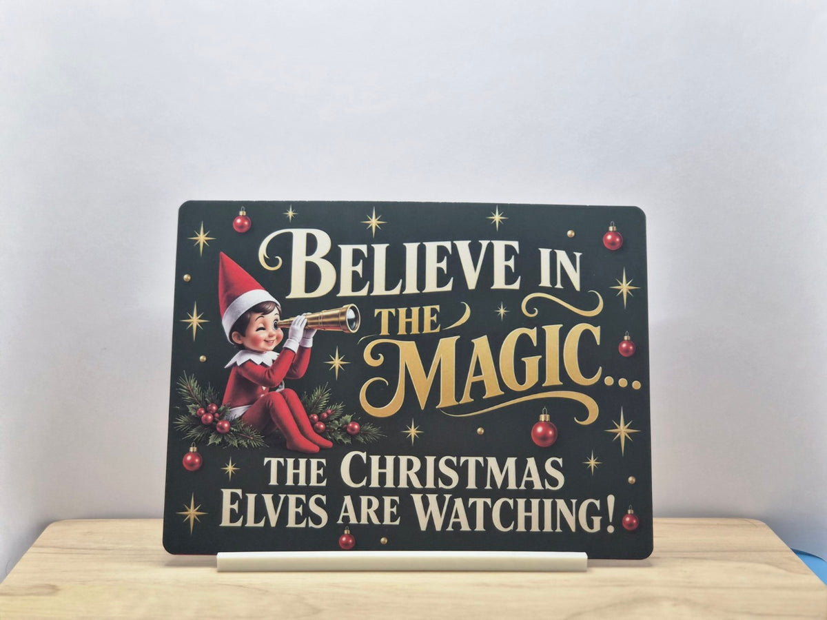 Christmas Elves Are Watching metal sign with an elf using a telescope, gold stars and red baubles, displayed in a white stand