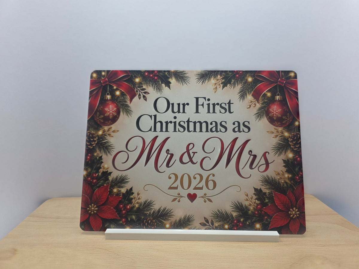 Our First Christmas as Mr and Mrs 2026 metal sign with red poinsettias and festive foliage, displayed in a white stand