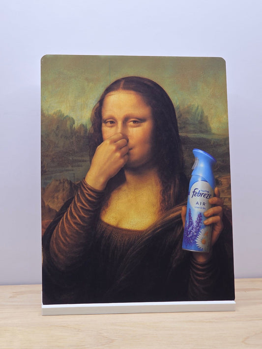 Mona Lisa air freshener parody metal sign showing her holding her nose and a blue aerosol can, displayed in a white stand