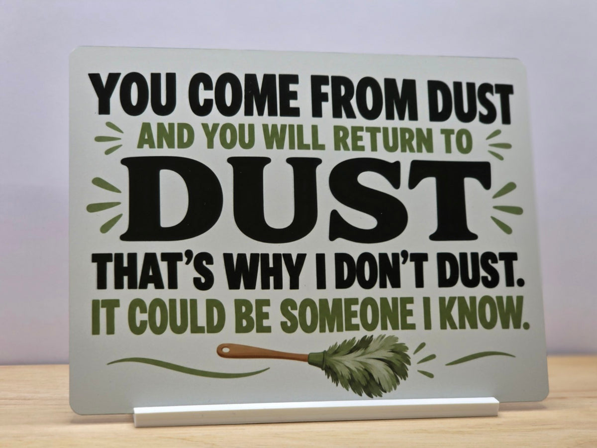 That's Why I Don't Dust funny metal sign with bold black lettering, green leaves and a feather duster, displayed in a white stand