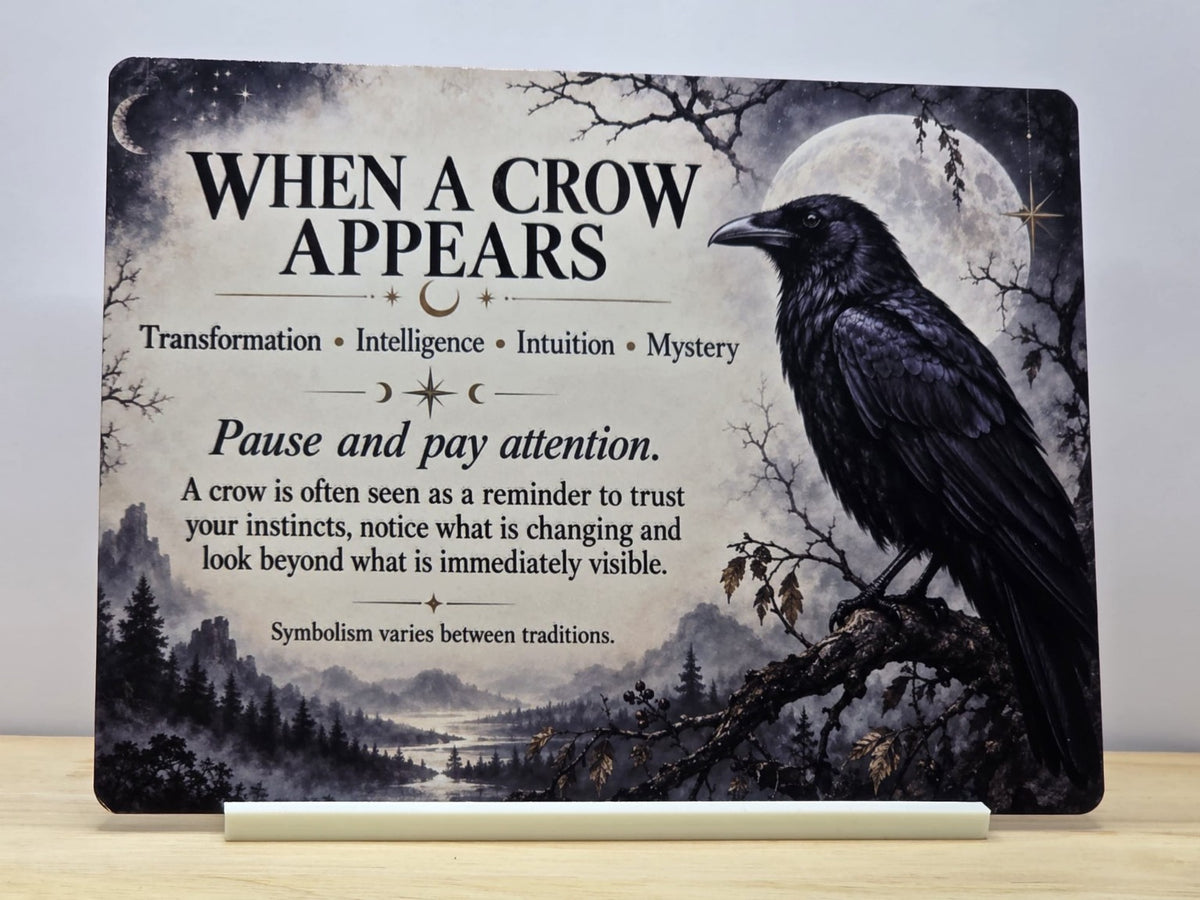 When a Crow Appears metal sign with a black crow, full moon and misty woodland, displayed in a white stand
