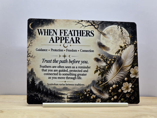 When Feathers Appear spiritual metal sign with floating feathers, pale flowers, a full moon and misty woodland