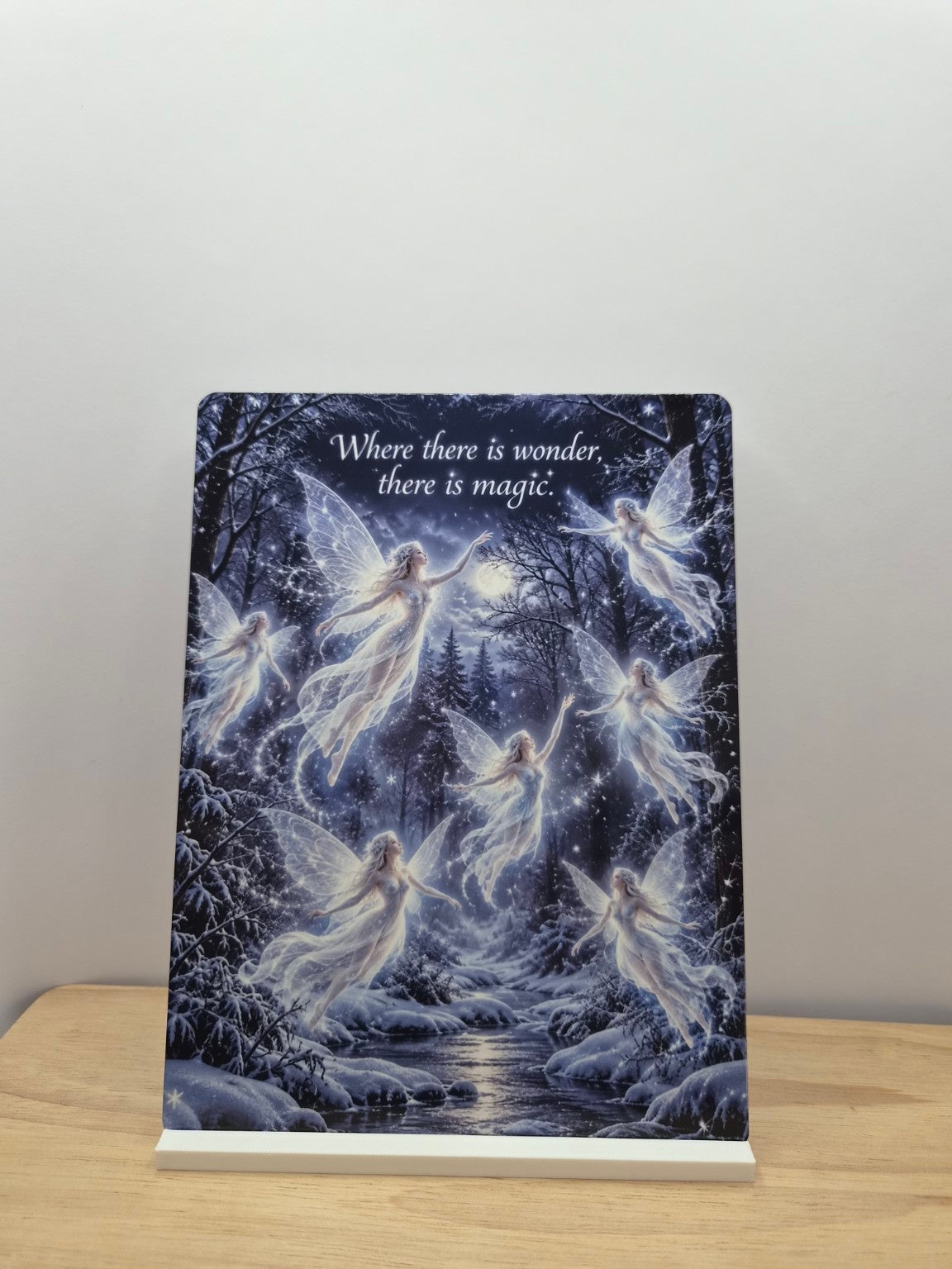 Where There Is Wonder fairy metal sign with a moonlit winter forest, glowing fairies and a stream, displayed in a white stand